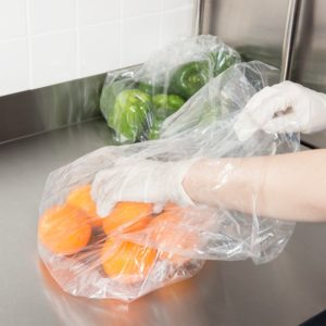 Person grabbing an orange from a bag with a glove